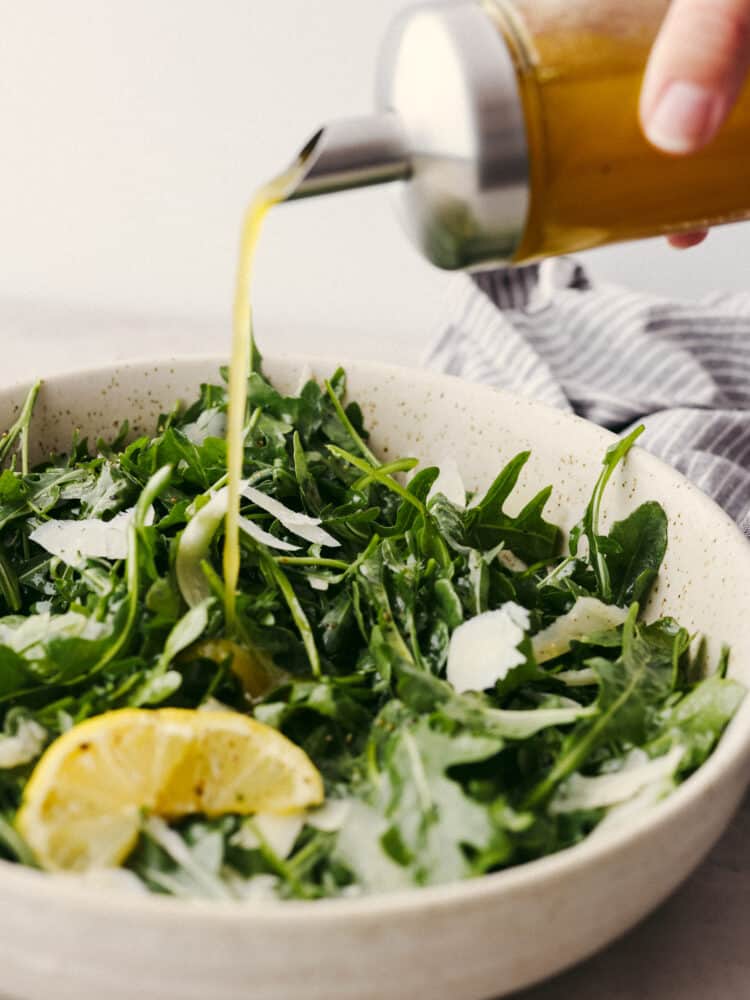 Lemon vinaigrette dressing being poured onto a arugula salad. 