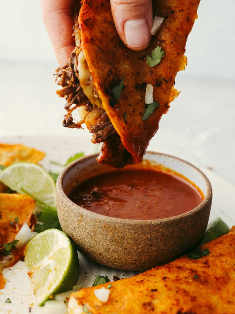 A birria taco being dipped into sauce. 