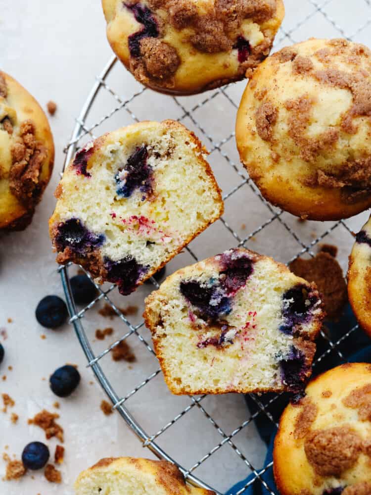 Blueberry muffins on a cooling rack cut iin half so that you can see the inside. 