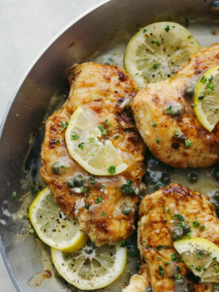 Close up of chicken picatta in a skillet with sauce, lemon slice, and capers.