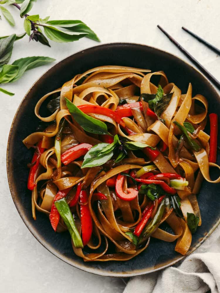 A bowl of drunken noodles ready to eat with chopsticks on the side. 