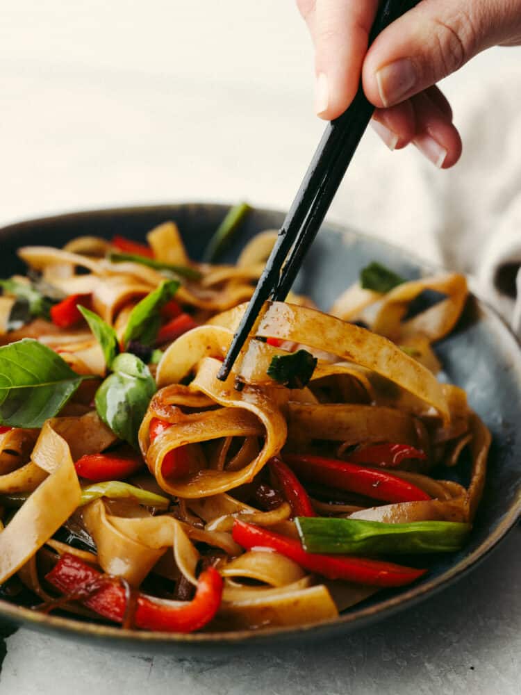 Drunken noodles in a bowl beaing grabbed with some black chopsticks. 