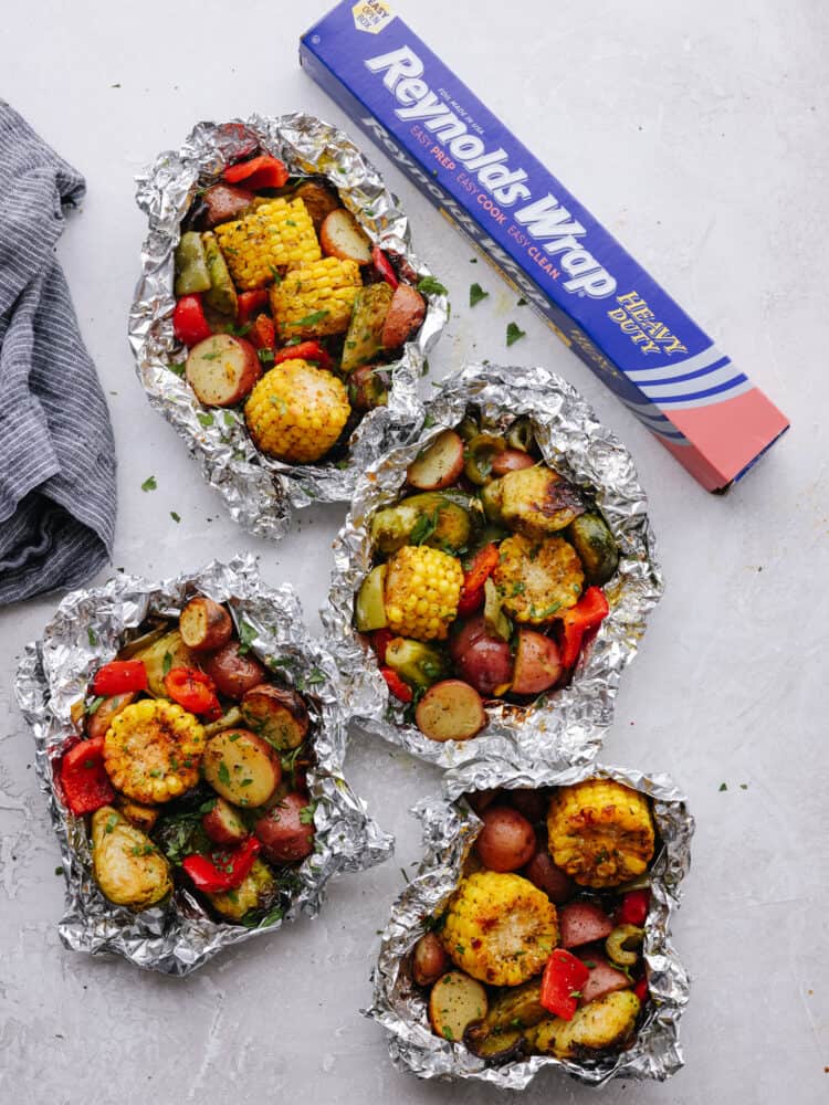 3 foild packs filled with cooked vegetables on a counter next to a box of Reynolds foil. 