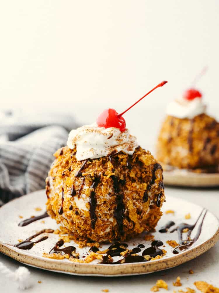 A globe-shaped fried ice cream topped with whipped cream, a maraschino cherry, and chocolate drizzle.