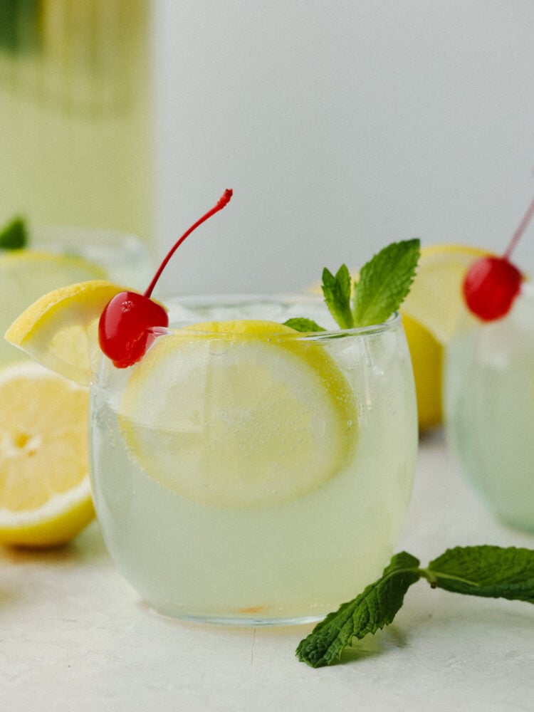 The side view of mint julet in a clear class cup garnished with a cherry, lemon and mint sprig. 