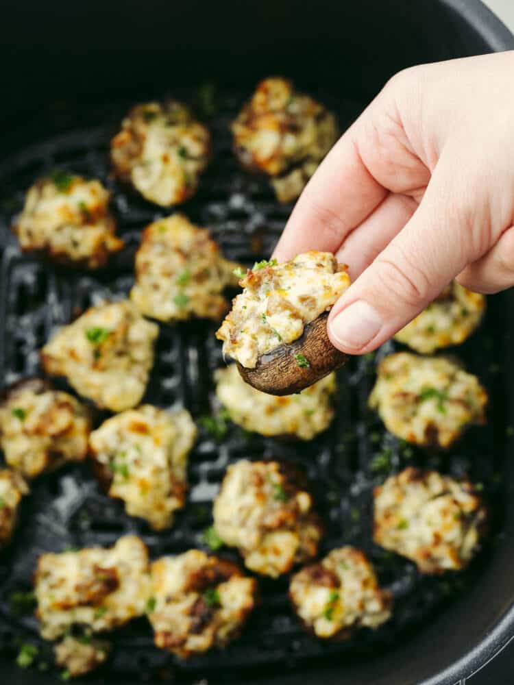 Picking up a cooked stuffed pepper out of an air fryer basket.