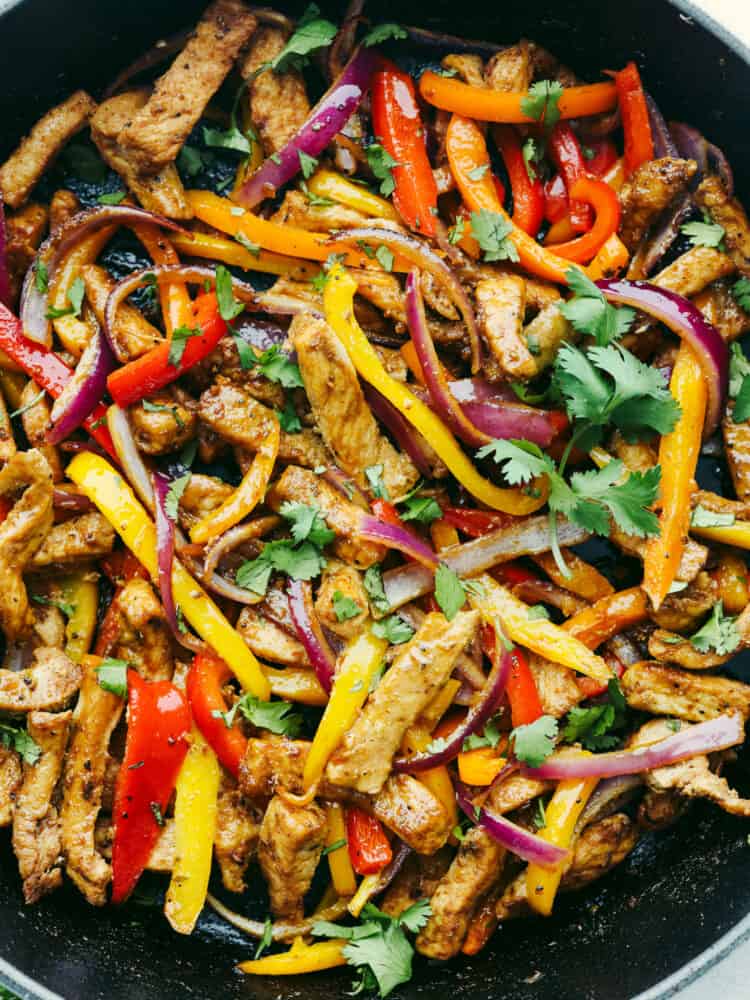 Close up photo of sliced and cooked pork, peppers, and onions.  Garnished with chopped cilantro.