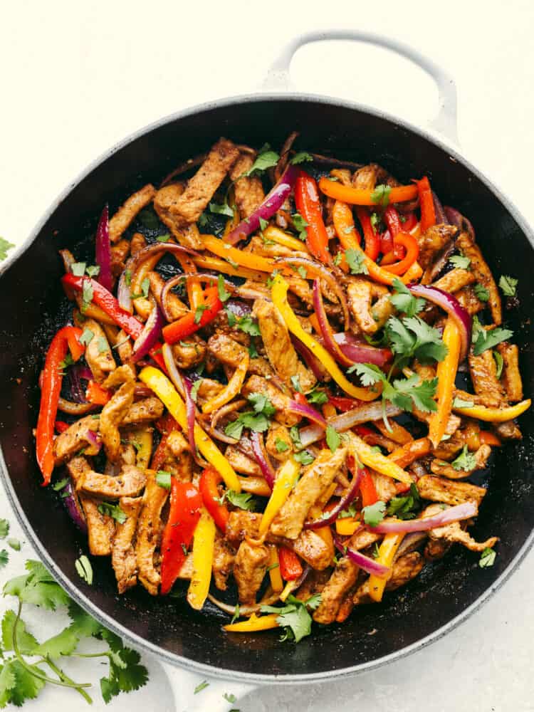 Cooked and seasoned pork, peppers and onions in a cast iron skillet, garnished with cilantro.