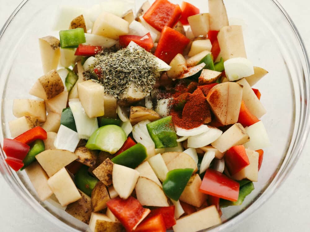 A clear, glass bowl with vegetables and seasonings ready to be mixed. 