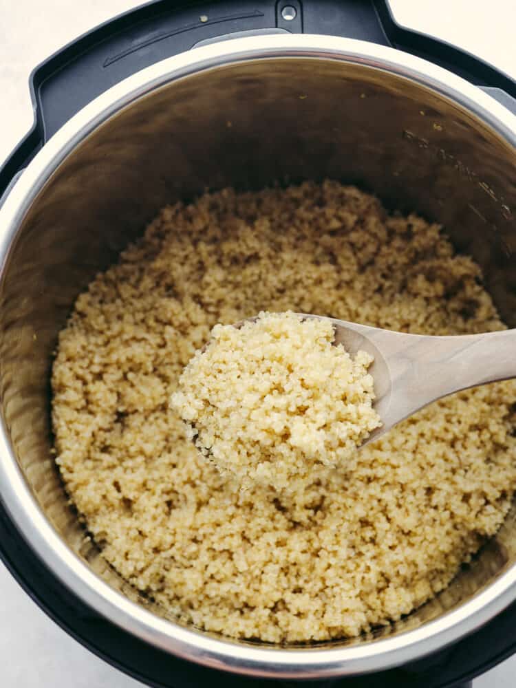 Cooked quinoa in an instant pot with a wooden spoon scooping some out. 