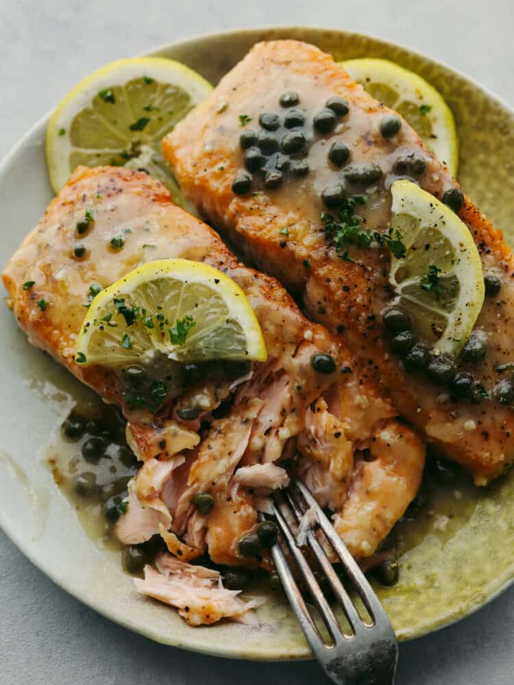 Salmn piccata on a plate with a fork cutting into the filet. 