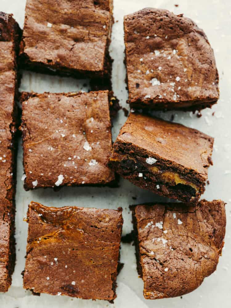 The top view of cooked brownies and sliced brownies on some parchment paper. 