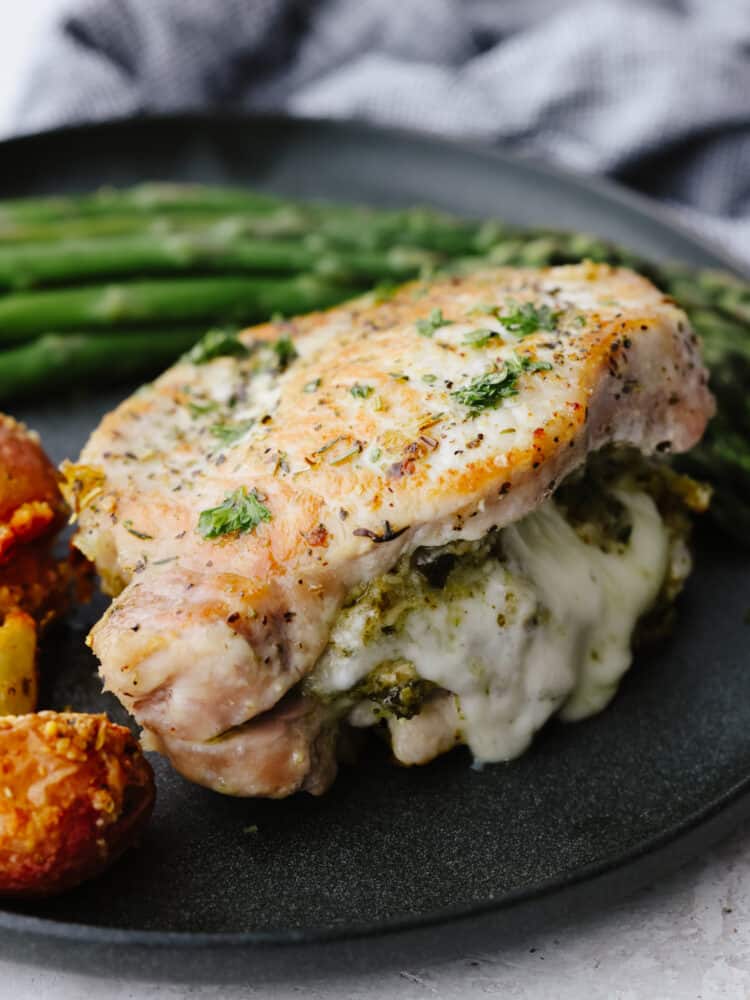 A close up shot of a post chop on a plate stuffed with cheese and pesto sauce. 