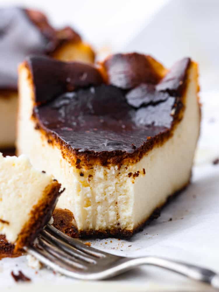 A close-up photo of a slice of Basque cheesecake.  A piece of cheesecake on a fork lying next to the slice of cheesecake.