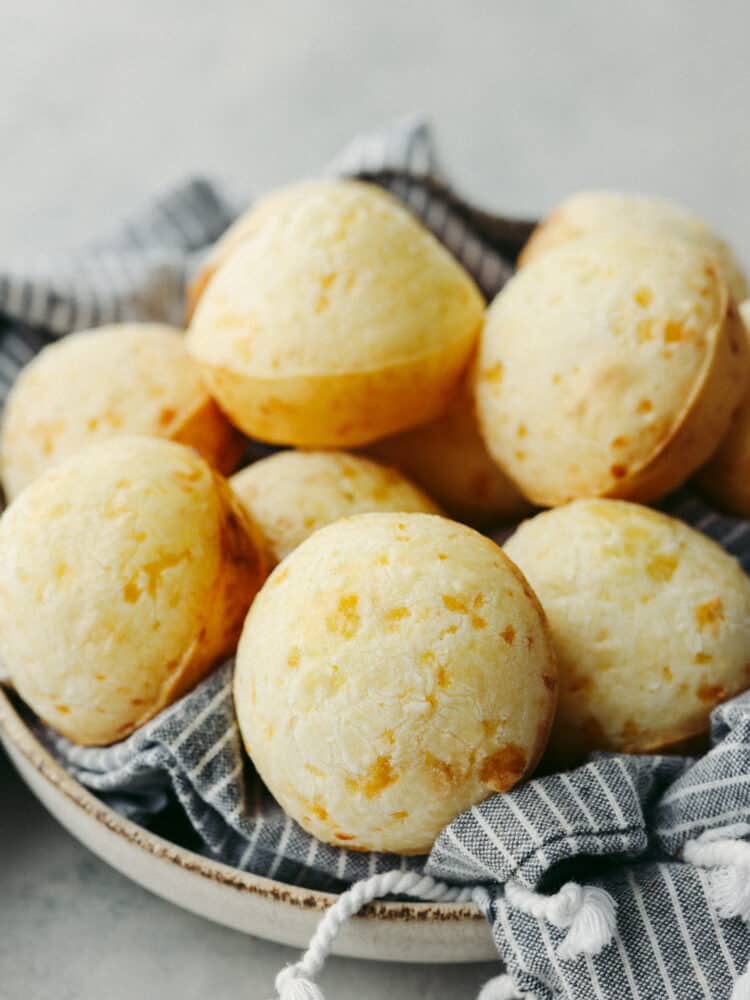 A stack of Brazilian cheese bread on a plate with a kitchen towel. 