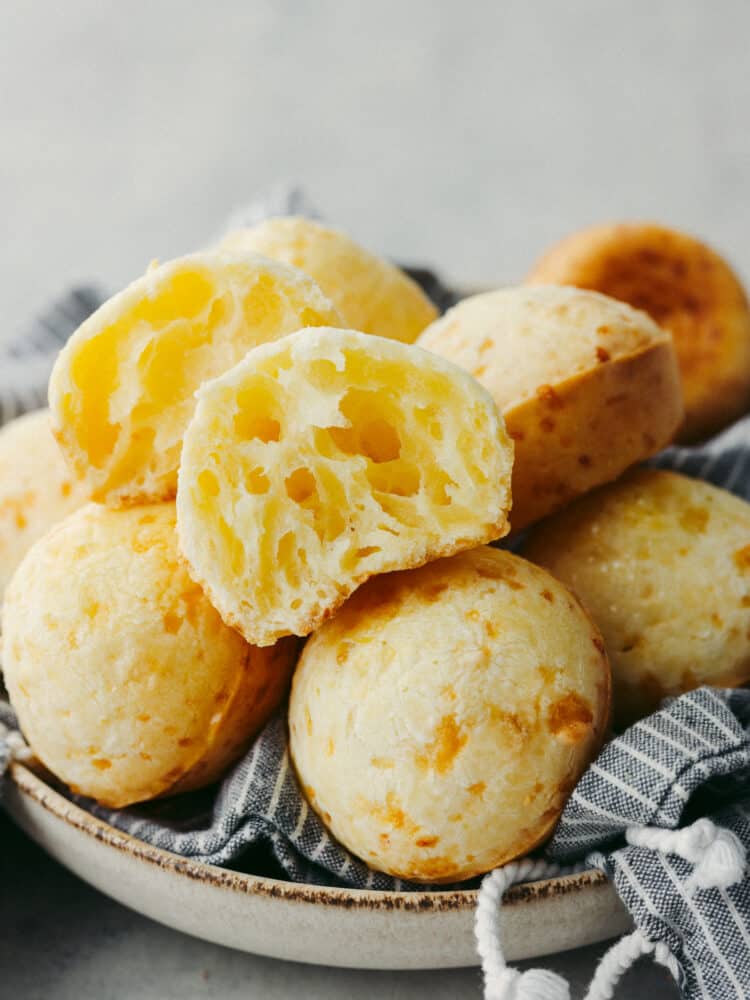 A stack of Brazilian cheese bread with the top on broken in half so that you can see inside. 