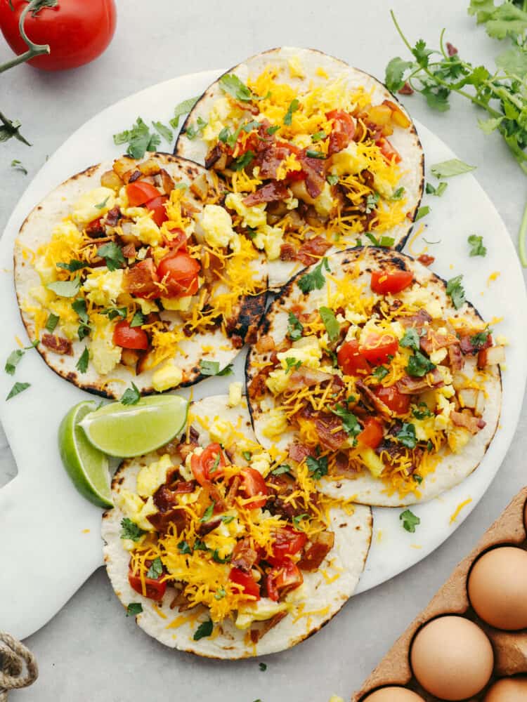 4 tortillas laying flat on a cutting board, each topped with breakfast taco filling. 