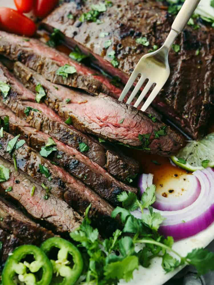 Close up photo of a fork holding a slice of arne asada meat.  Garnished with cilantro and onion and jalepeno on the side.