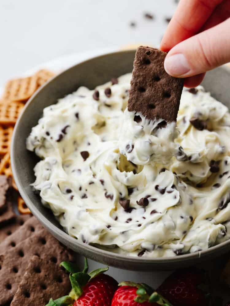 A close up of a chcolate cracker being dipped into chocolate chip cookie dough dip. 