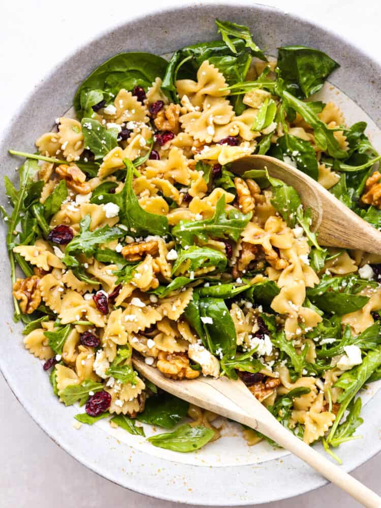 Top-down view of cranberry feta pasta salad being tossed with two wooden spoons.