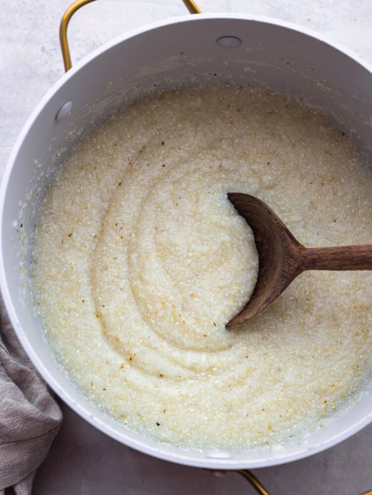 A pot of cooked grits with a wooden spoon. 