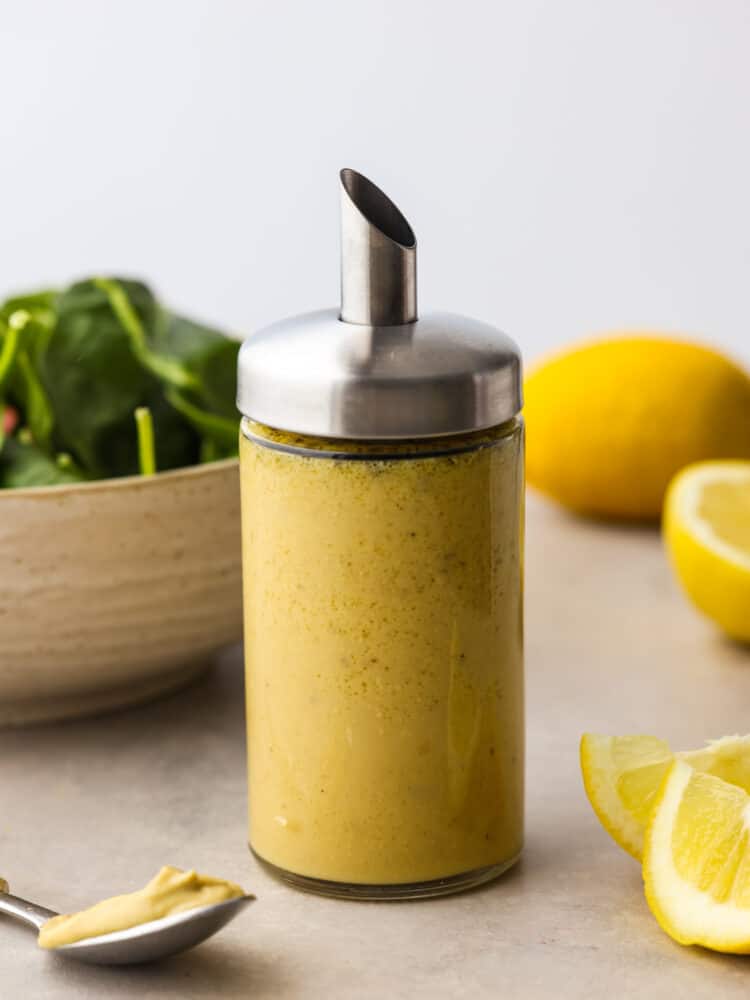 Homemade honey mustard dressing in a glass container with a metal spout.