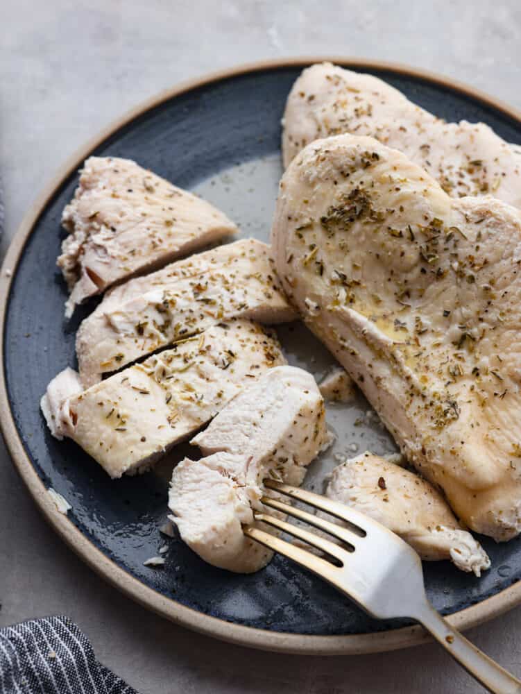 Instant pot frozen chicken cooked, seasoned and ready to eat. Sliced and placed on a blue plate with a fork. 