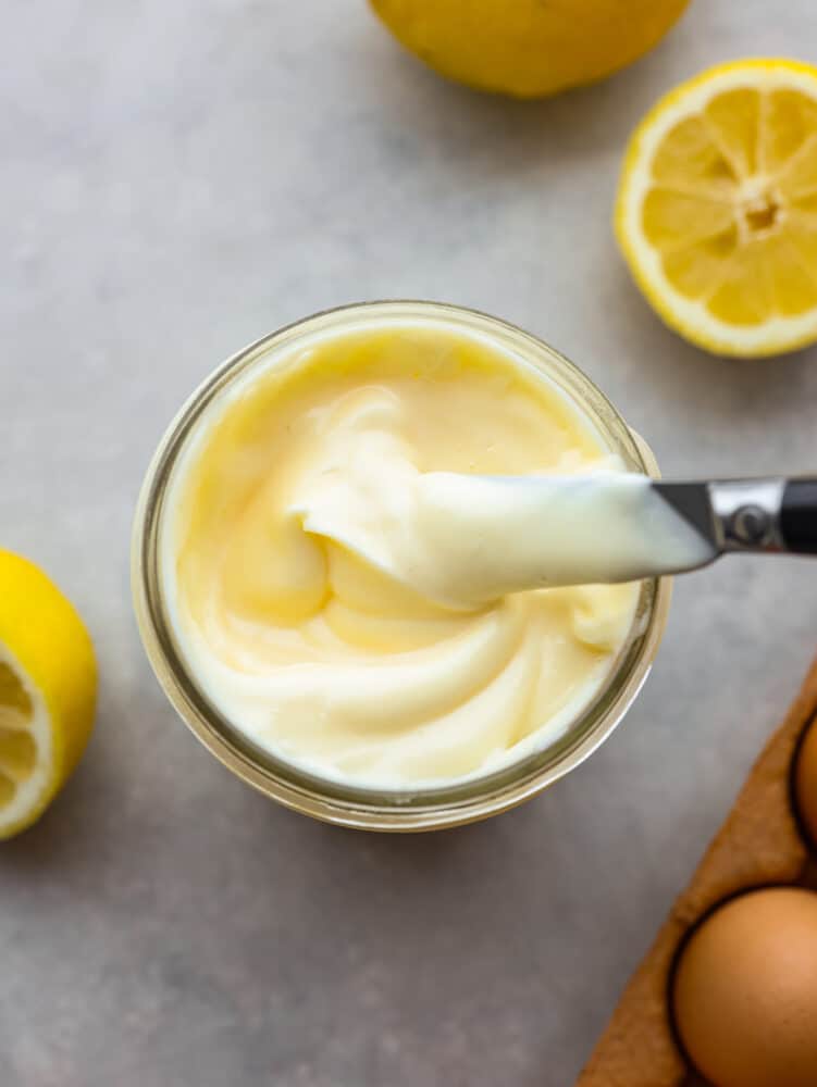 Top view photo of mayonnaise in mason jar with a knife covered in mayonnaise and lifting out of the jar.