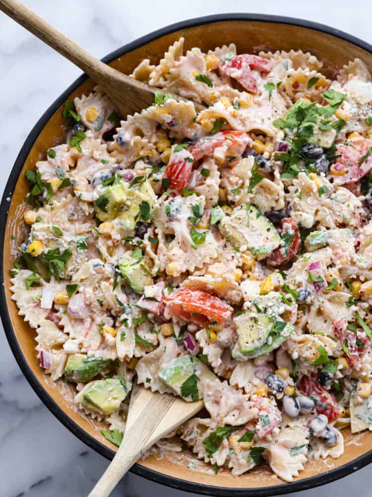 A bowl of Mexican pasta salad with a wooden spoon. 