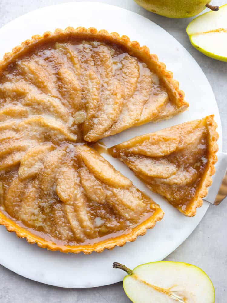 The top view of a pear tart with a slice being taken out with a pie server. 