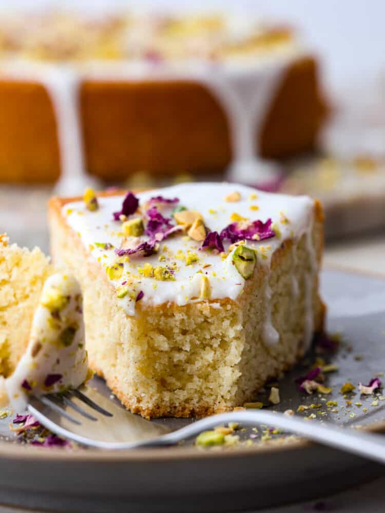 The side view of a slice of cake on a plate with a fork with a bite taken out. 