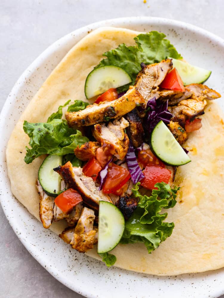 A pita on a plate topped with veggies and chicken shawarma. 