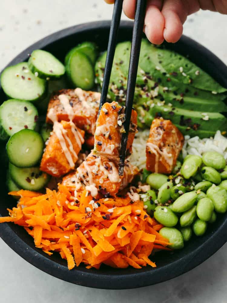 Top view of the assembled salmon rice bowl with chopsticks lifting out the salmon from the bowl.