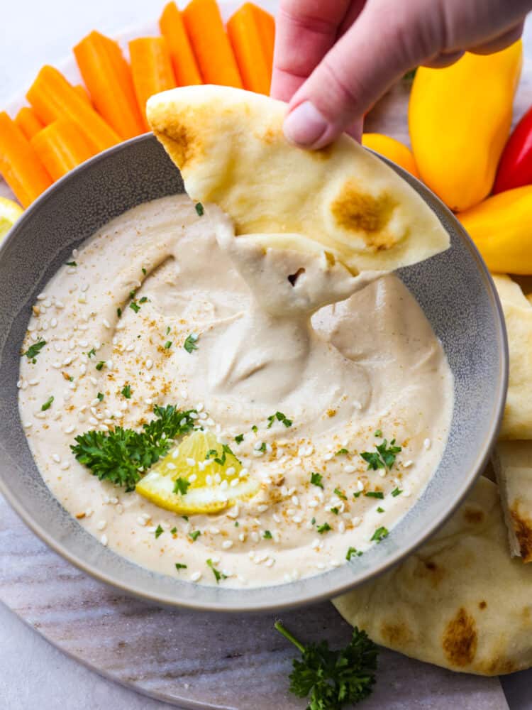 A triangle of pita bread being dipped into a bowl of tahini sauce. 