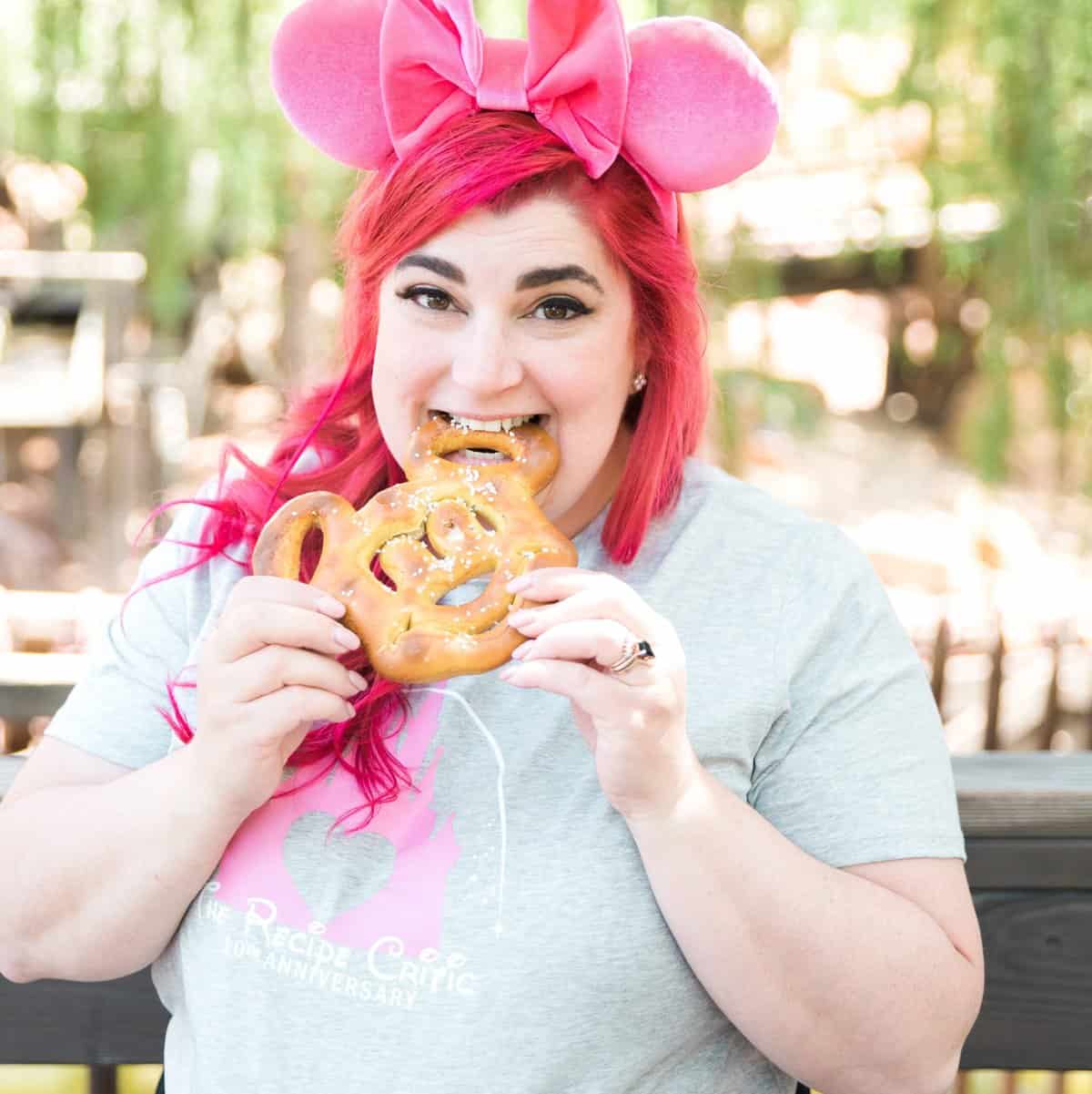 A woman eating disneyland food, a mickey pretzel. 