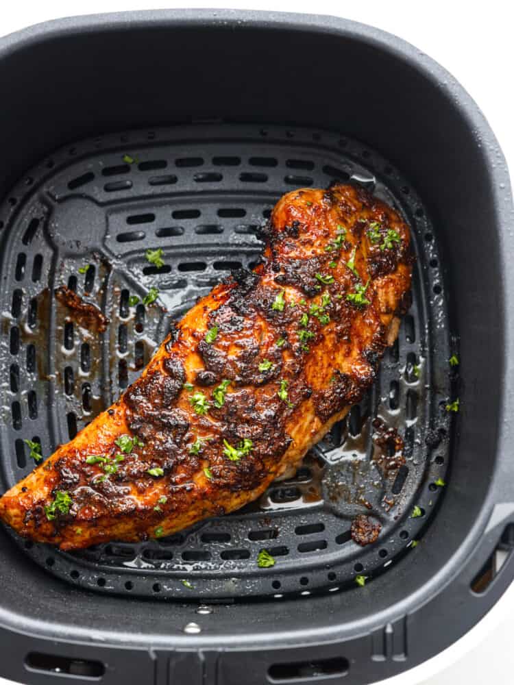 Top view of finished cooked pork tenderloin in the air fryer basket and garnished with fresh parsley.