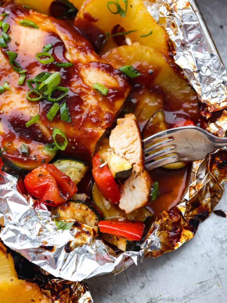 A close up of a fork cutting into the grilled Hawaiian barbecue chicken thats in a foil packet. 