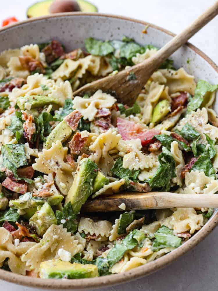 A close up of BLT Avocado Pasta Salad with a wooden spoon. 