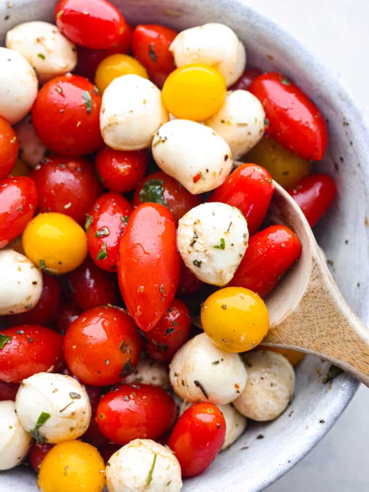 Cherry tomato salad in a bowl being served with a wooded spoon. 