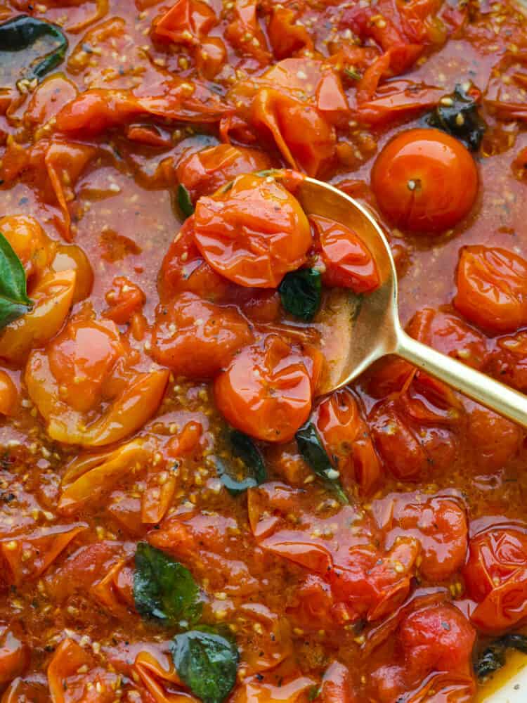 Close view of cherry tomato sauce with a gold spoon lifting up the sauce.