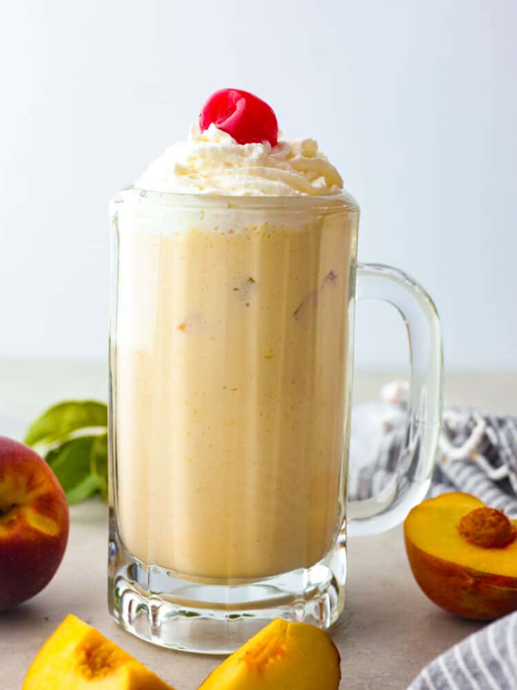 A peach milkshake in a glass mug, garnished with a cherry.