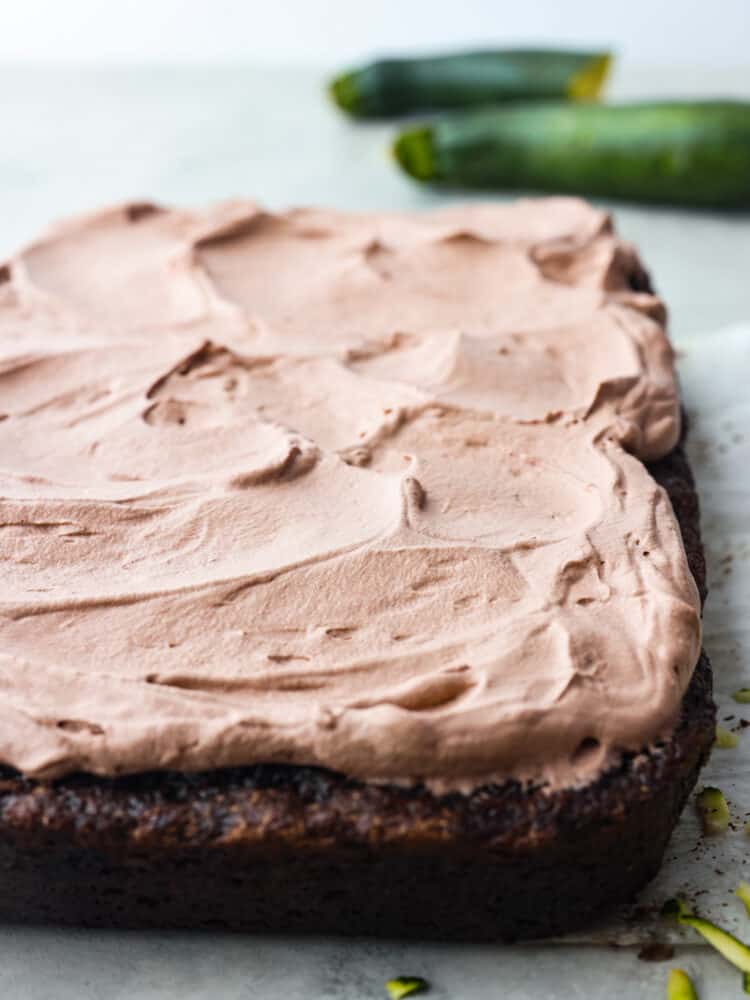 The side view of a chocolate zucchini cake on parchment paper with the whipped topping on top. 