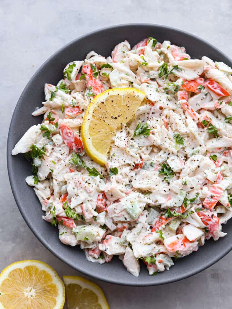 Top-down view of crab salad in a gray bowl, garnished with a lemon.