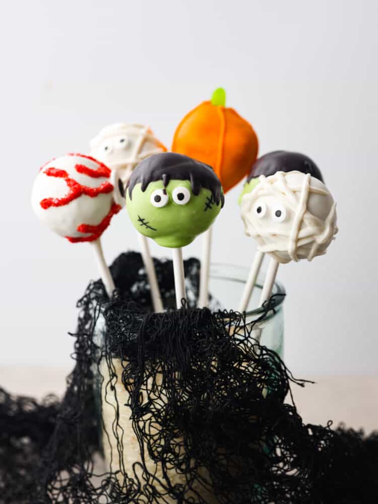 5 donut hole pops decorated like Halloween characters in a glass jar.