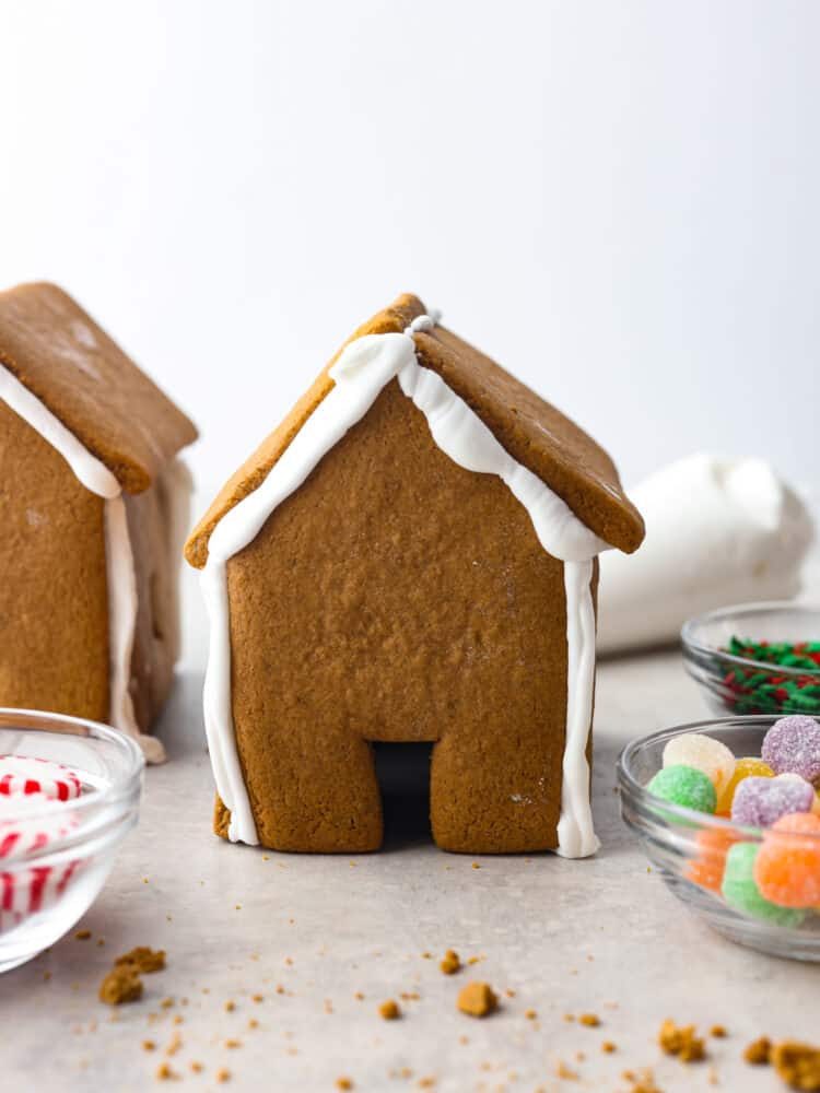 Gingerbread house with bowls of candy around it and another house in the background.