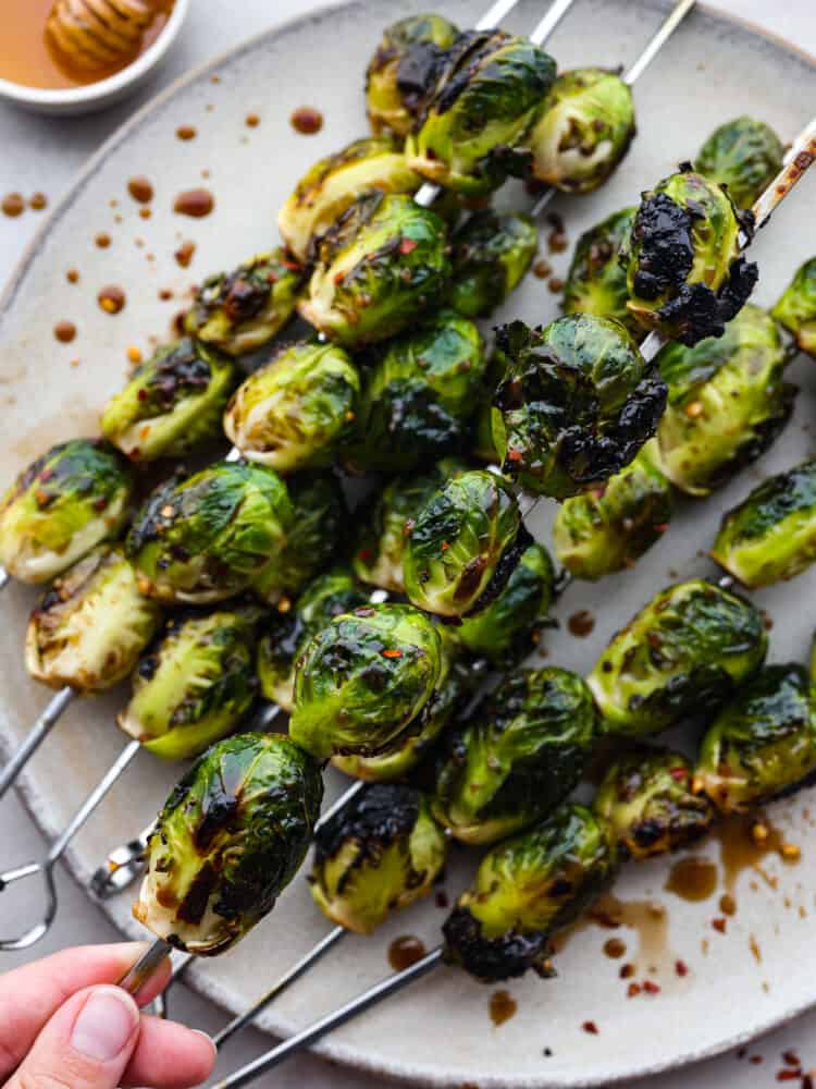 A skewer of grilled brussels sprouts being picked up.