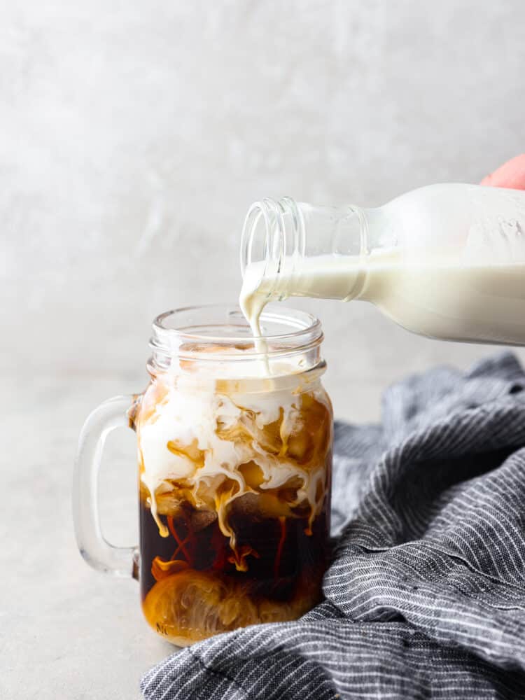 Half and half being poured into a glass cup filled with soda. 