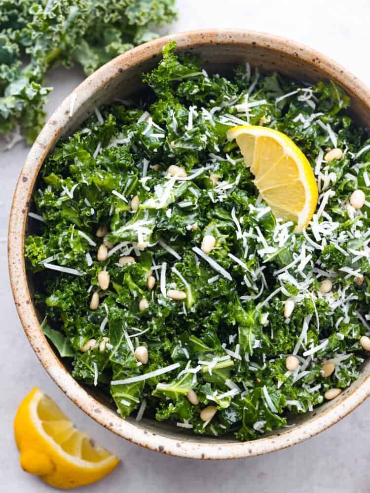 Top-down view of kale salad in a brown serving bowl, garnished with a lemon.