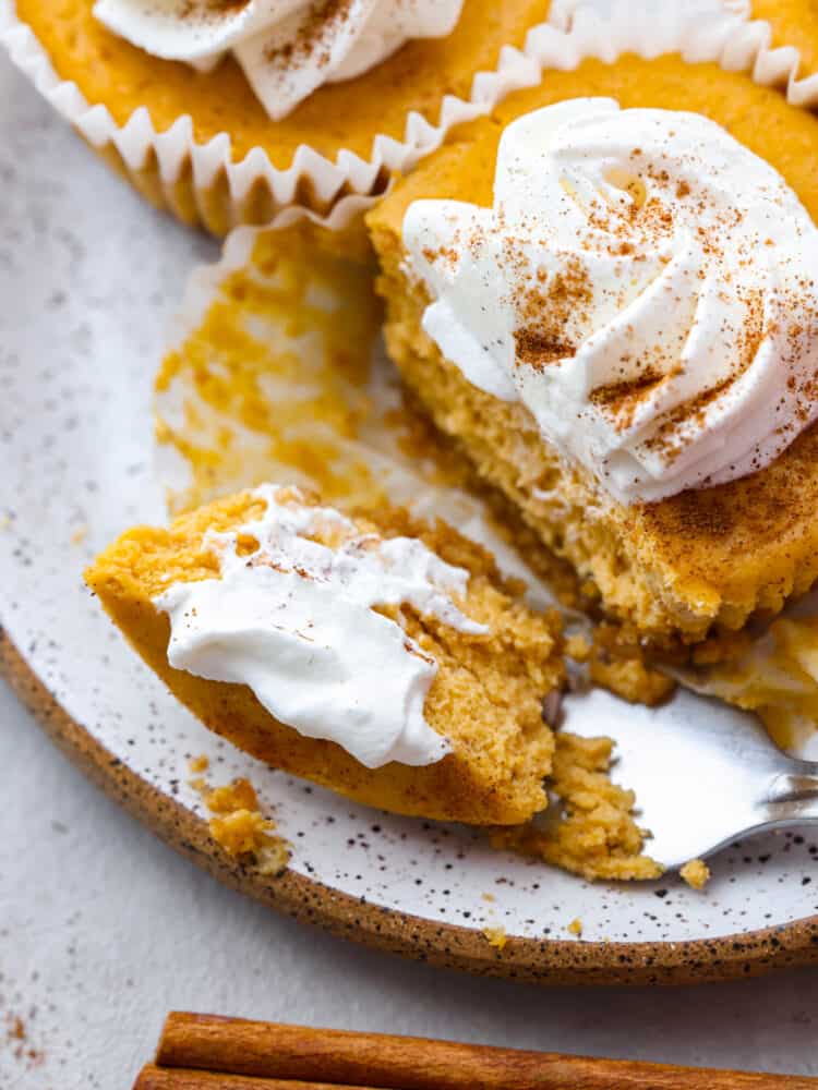 Closeup of cheesecake topped with whipped cream and dusted with cinnamon. There is a piece cut out by a metal fork.