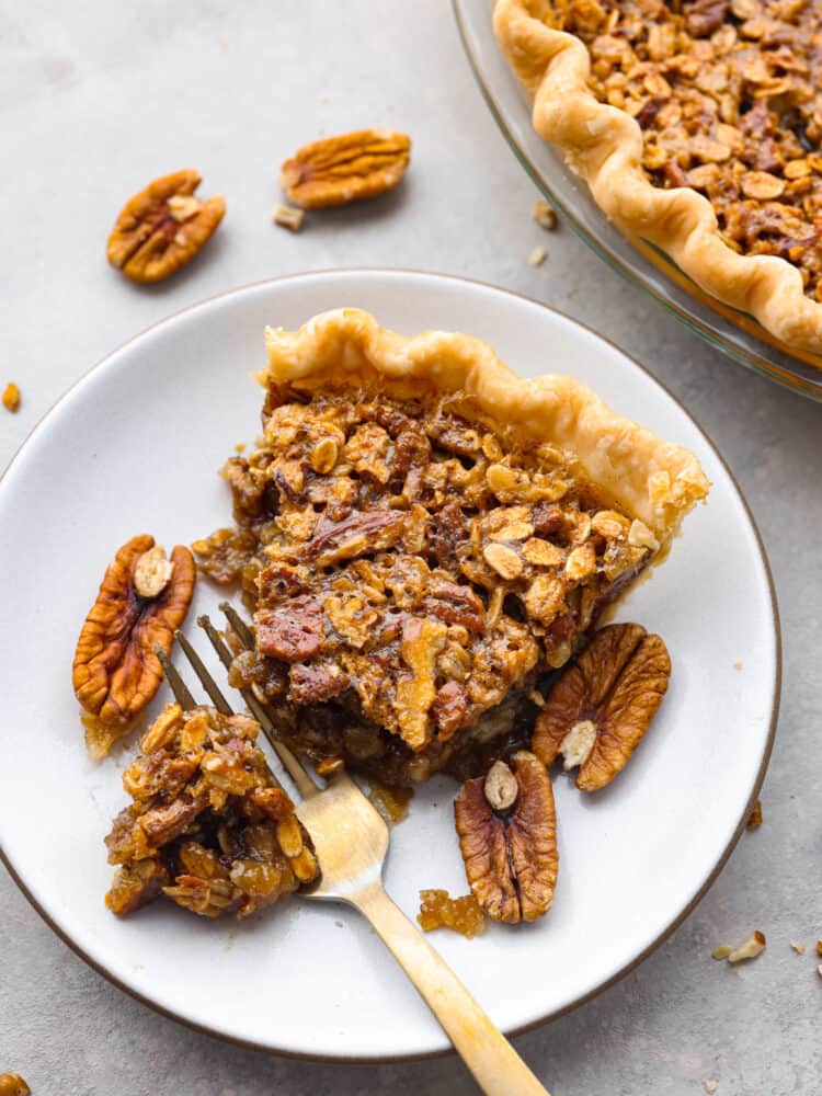 A slice of oatmeal pecan pie on a plate with a gold fork cutting out a piece to eat. 